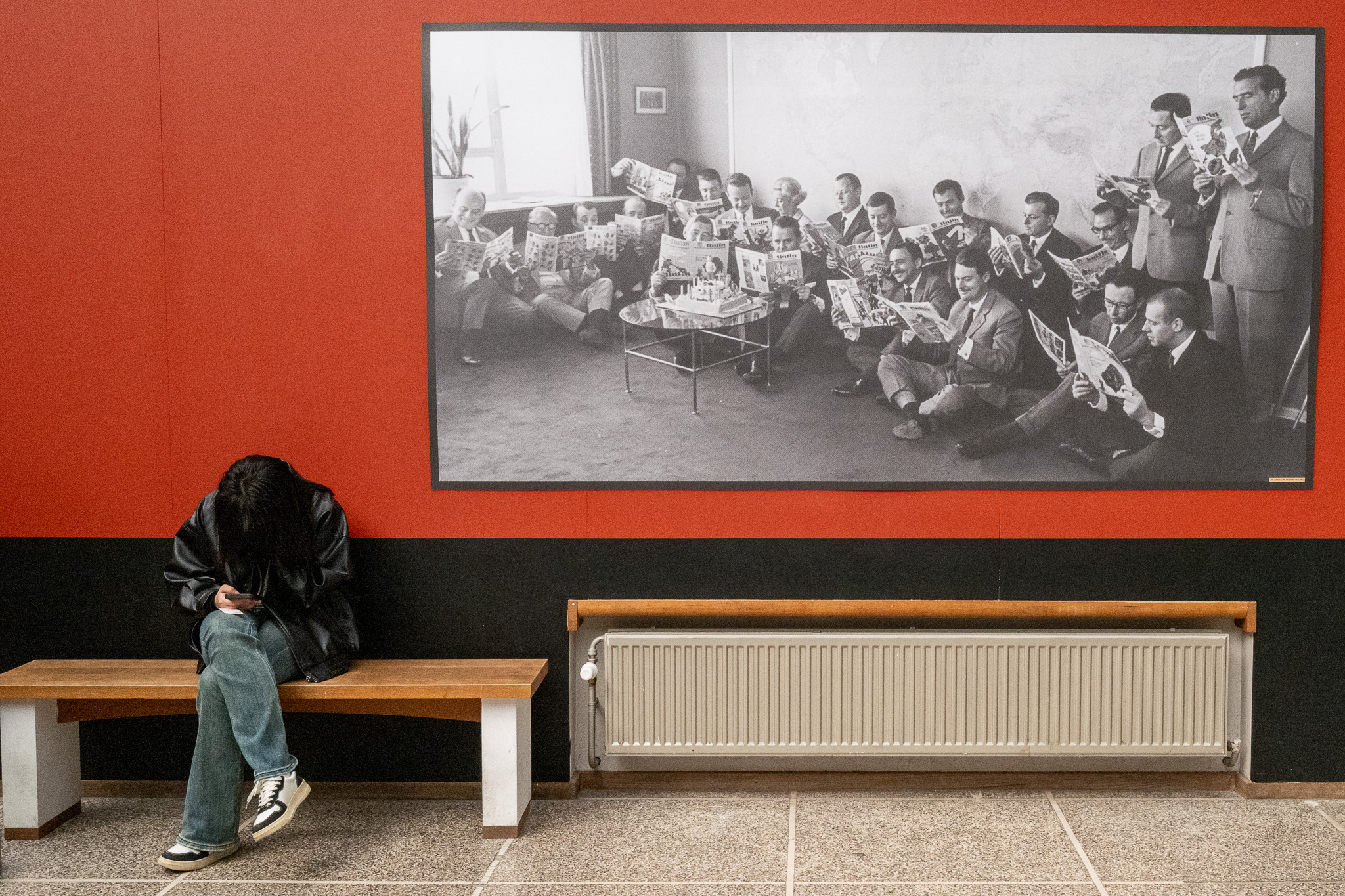 A kid on his smartphone, sitting next to a vintage photograph of people reading newspapers